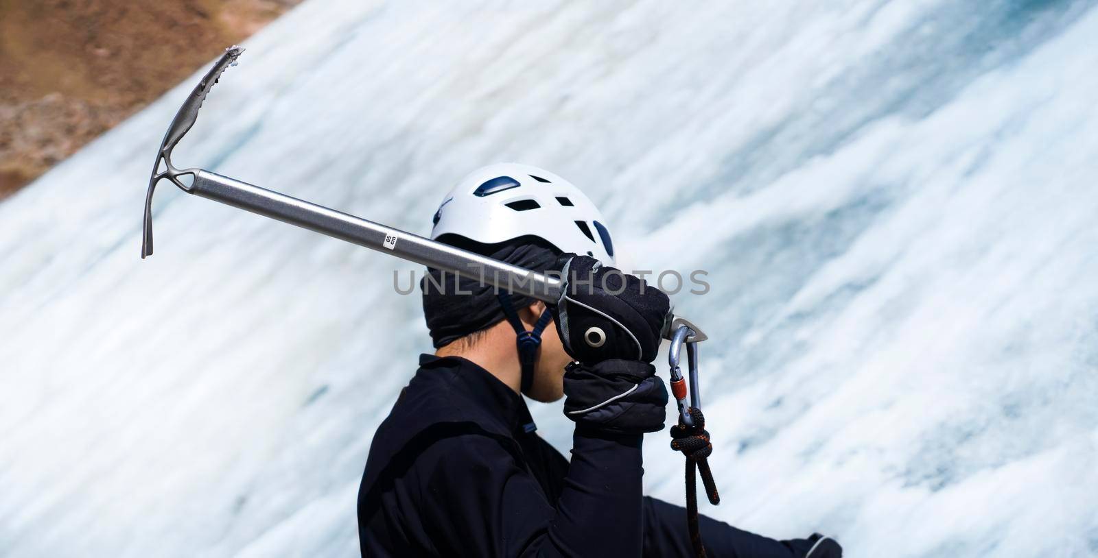 A young man traveler uses an ice ax while hiking in the mountains, a hiker with climbing equipment, in a helmet, crampons climbs to the top of a snow-capped mountain.