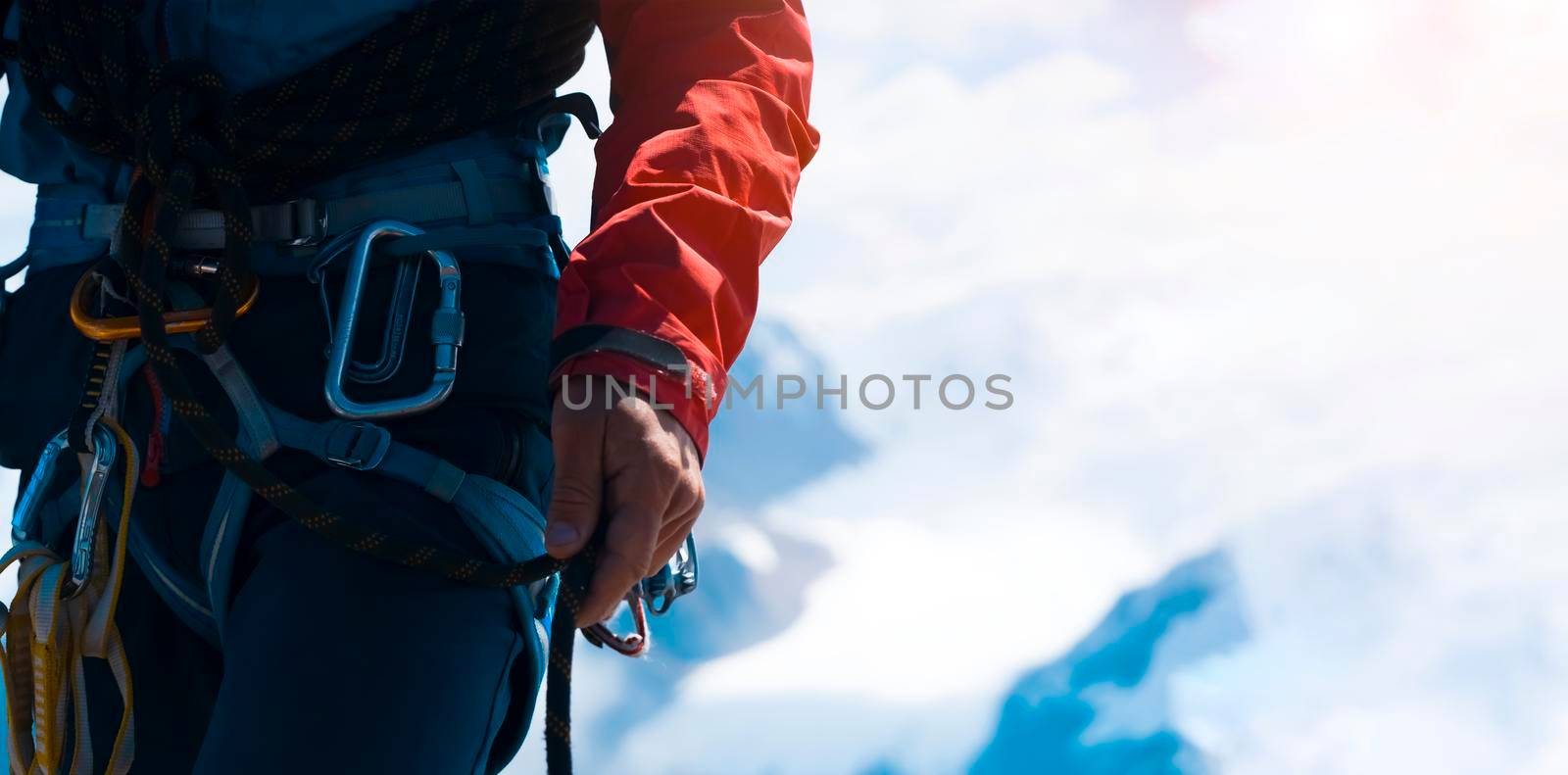 Young man traveler alpinist climbs to the top of a snowy mountain with climbing equipment, harness, carbines, rope.