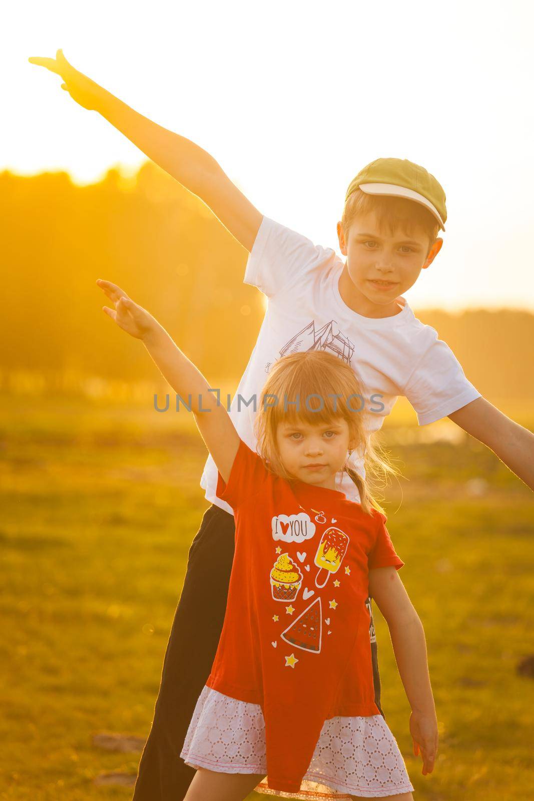Children play an airplane and laugh against the backdrop of the setting sun. High quality photo