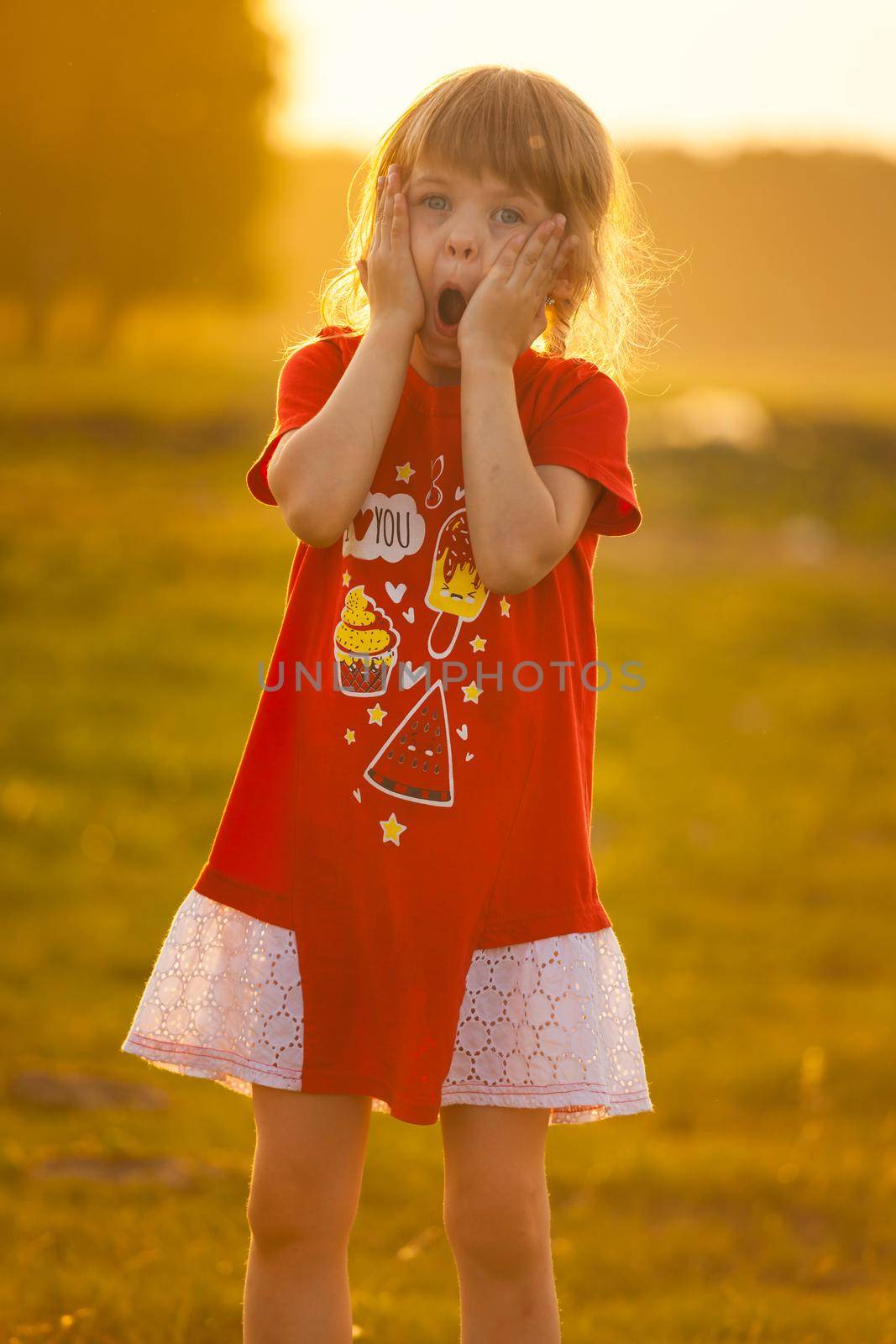 Little girl is very surprised against the backdrop of the setting sun. High quality photo