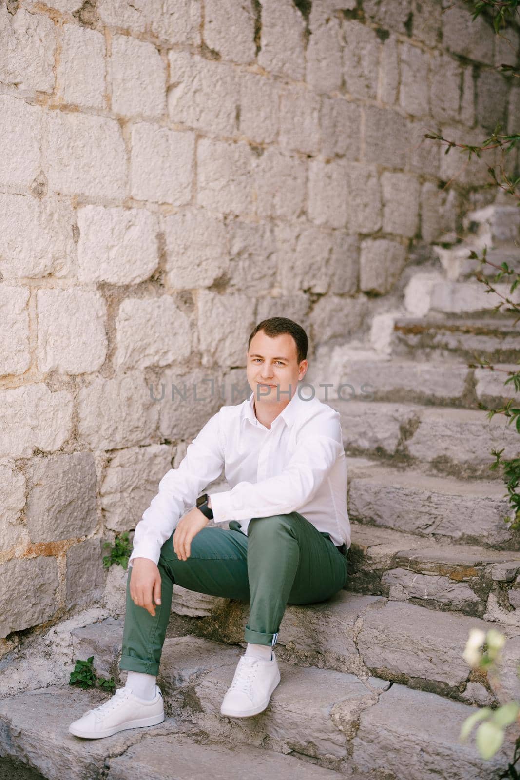 Man in a white shirt sits on stone steps near a gray brick wall. High quality photo