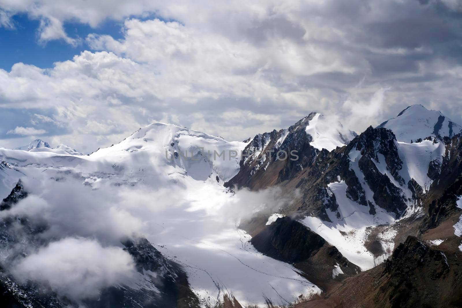 Stunning majestic landscape with snow-capped mountains and glaciers among the clouds on a sunny day.