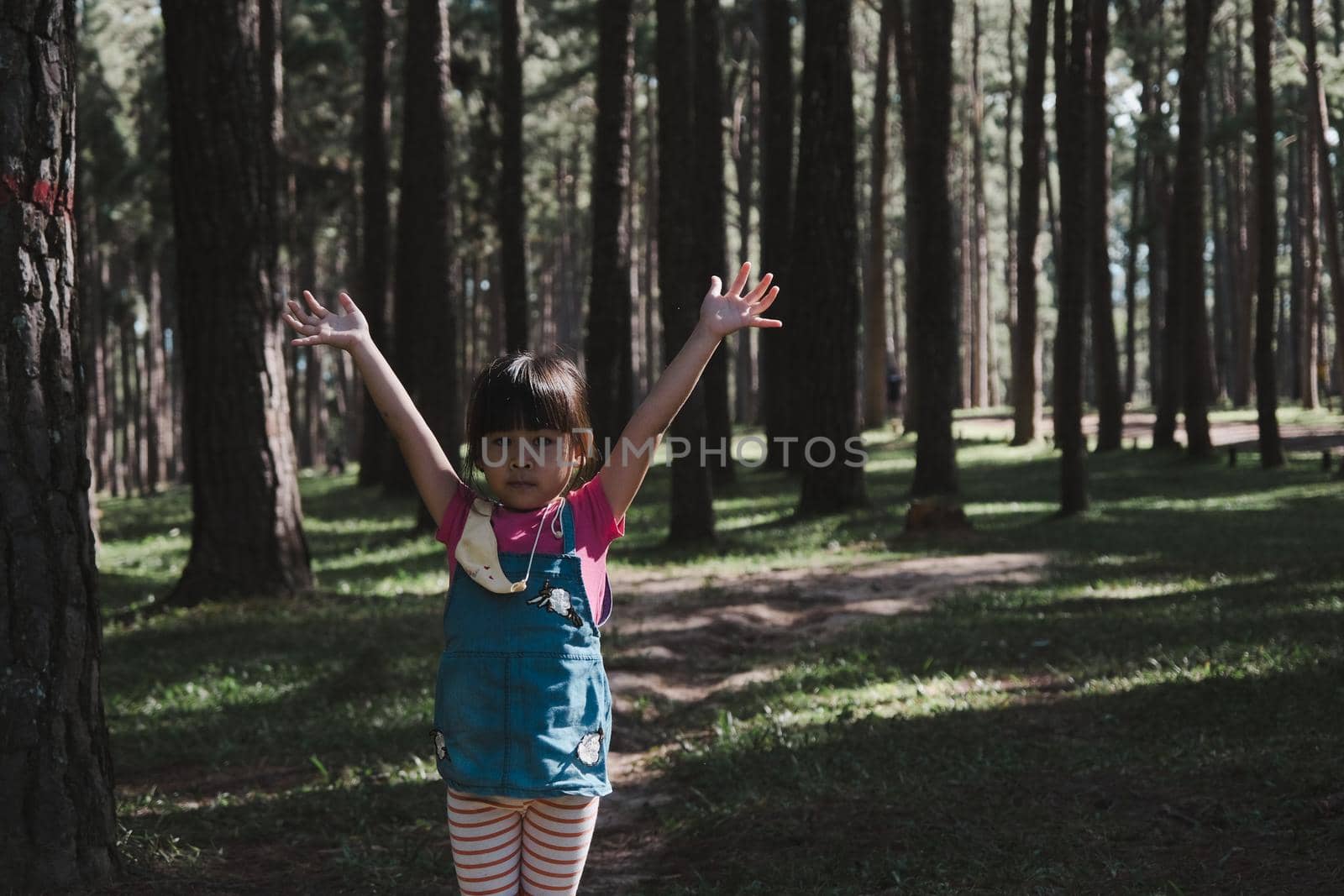 Active little girls running in the pine forest on a warm summer day. Happy girl smiles and laughs while spending time with her family in the park on vacation. by TEERASAK