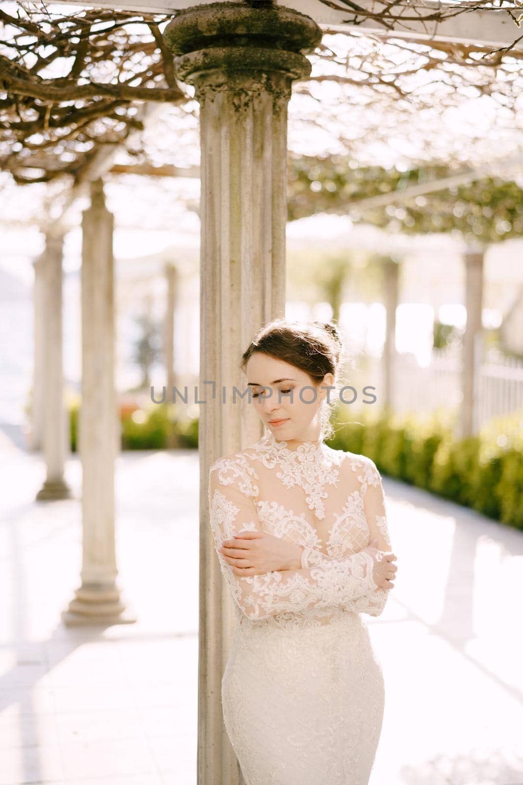 Bride in a dress stands near a column in an old patio. Portrait. High quality photo