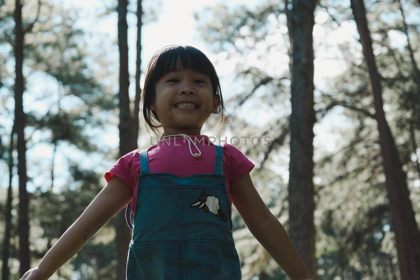 Active little girls running in the pine forest on a warm summer day. Happy girl smiles and laughs while spending time with her family in the park on vacation. by TEERASAK