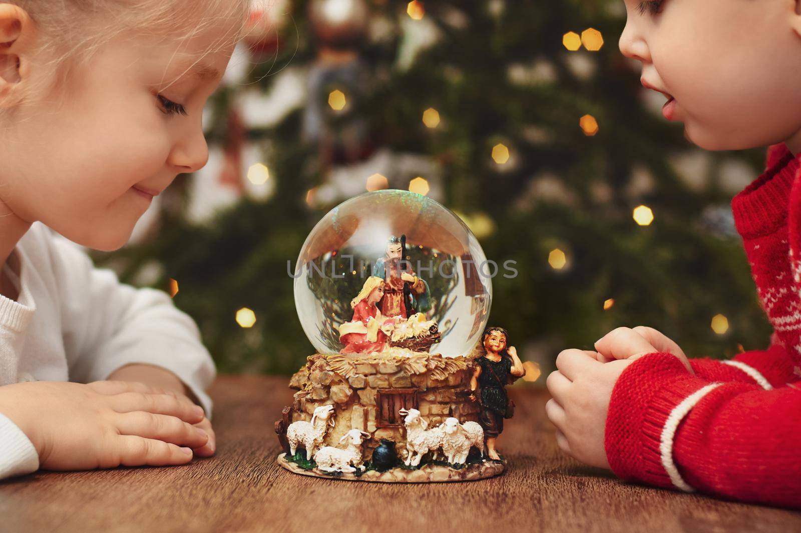 Children looking at a glass ball with a scene of the birth of Jesus Christ near christmas tree