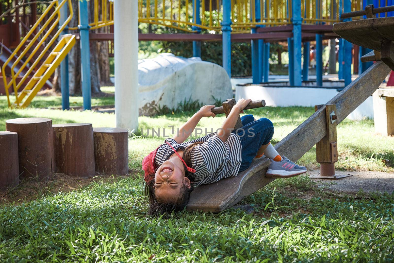 Active little girl playing on a seesaw in the outdoor playground. Happy child girl smiling and laughing on children playground. Play is learning in childhood. by TEERASAK