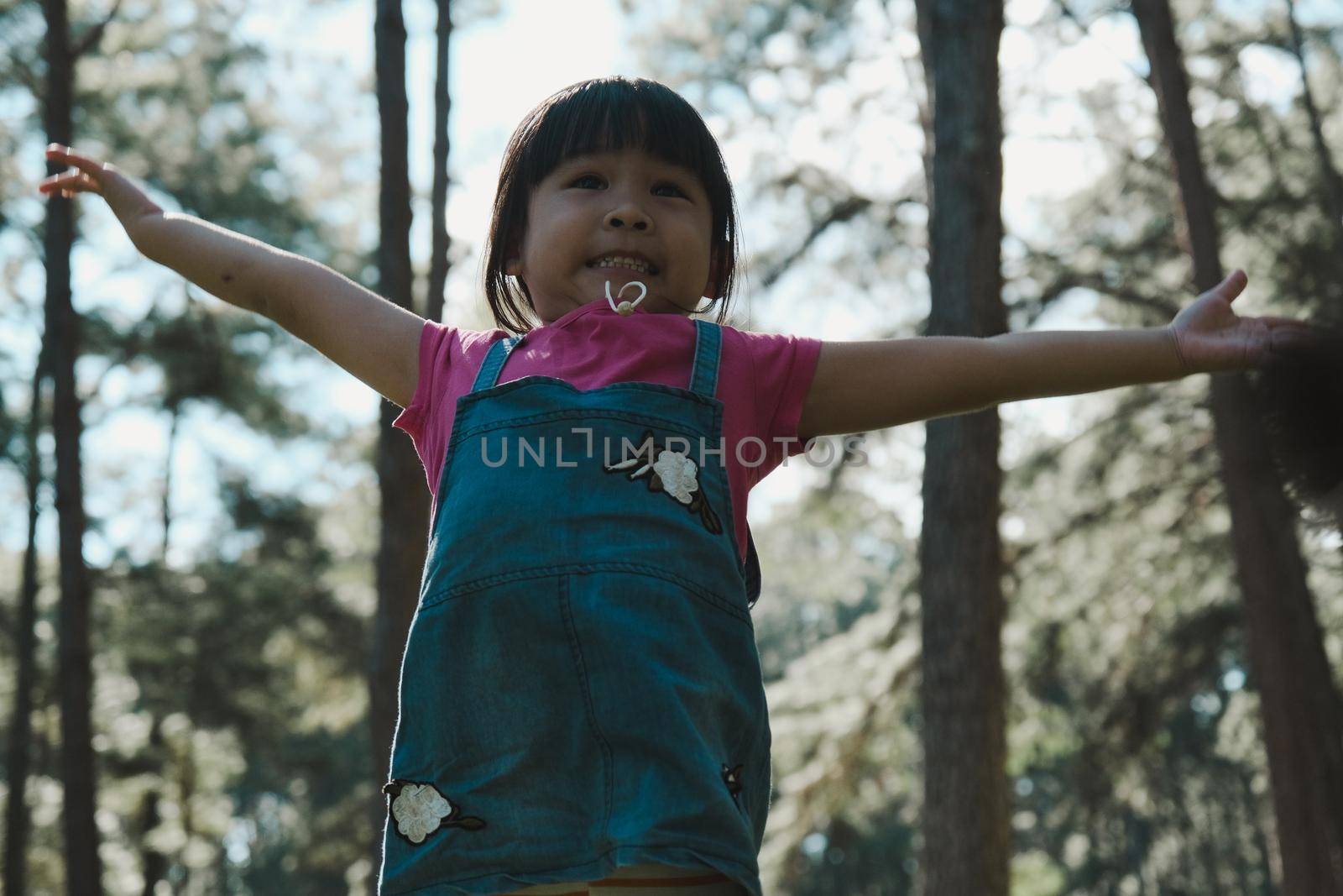 Active little girls running in the pine forest on a warm summer day. Happy girl smiles and laughs while spending time with her family in the park on vacation.