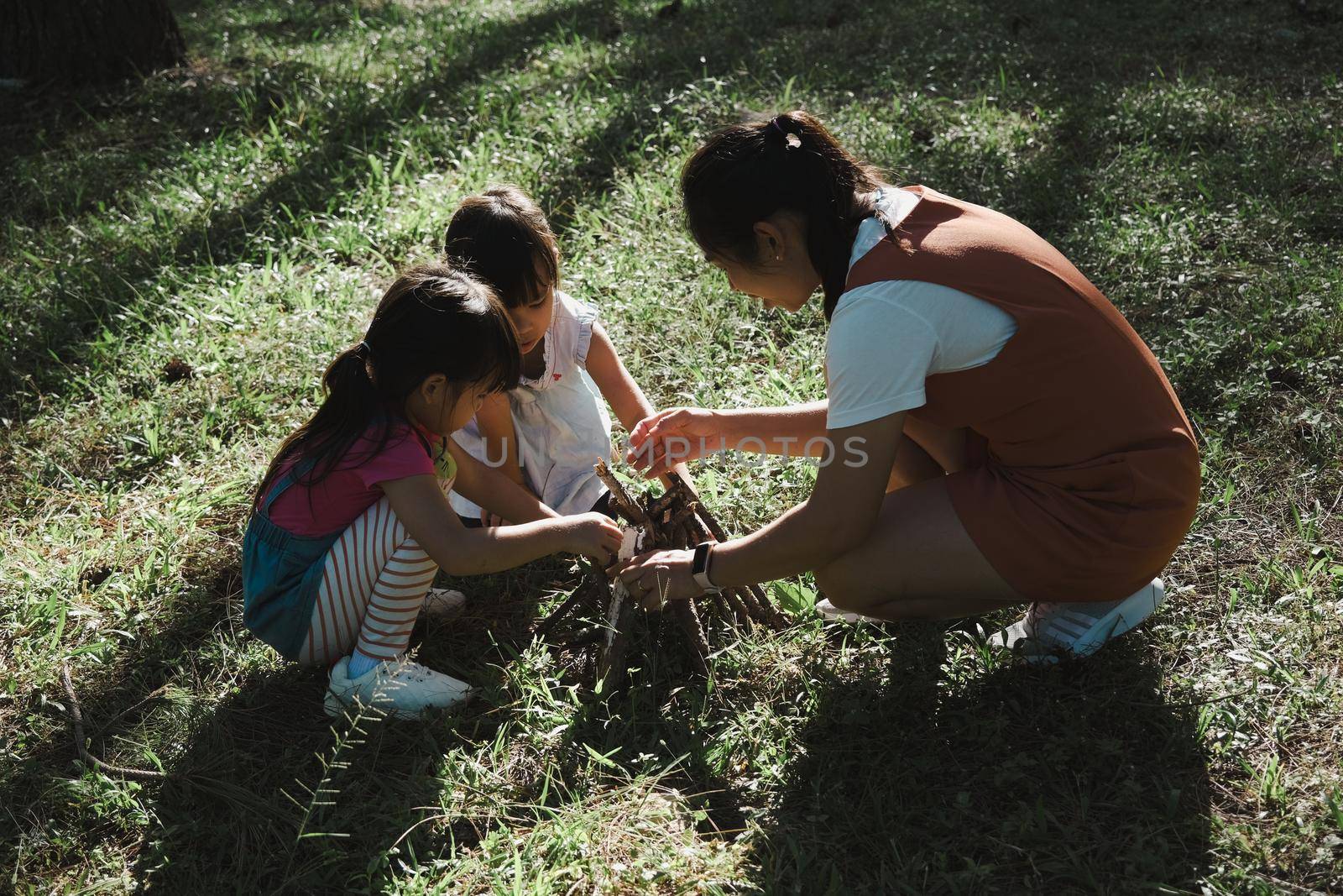 Mother and two daughters collecting firewood and kindling bonfire at camping place in forest. Family and children making campfire on nature woods. Family camping, spending time together on vacation. by TEERASAK