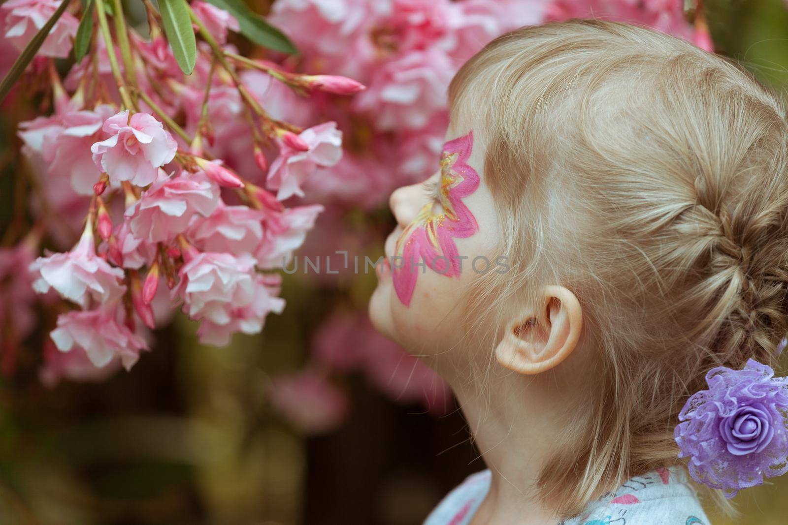 A girl with makeup on her face is sniffing pink flowers. by gordiza