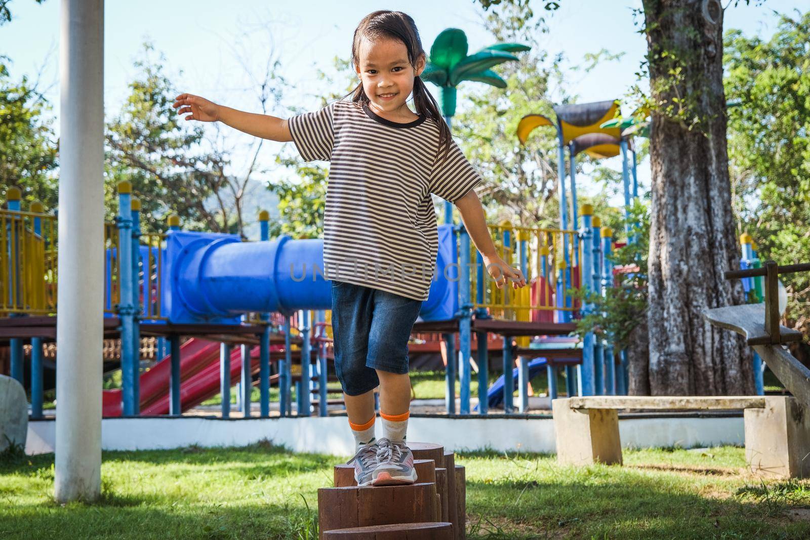 Active little girl walking on balance beam in the outdoor playground in the park. Happy child girl having fun in children playground. Play is learning in childhood.