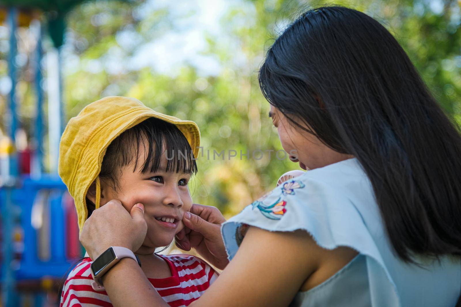 Young mother puts a hat on her daughter in the summer park. Family spends time together on vacation. by TEERASAK