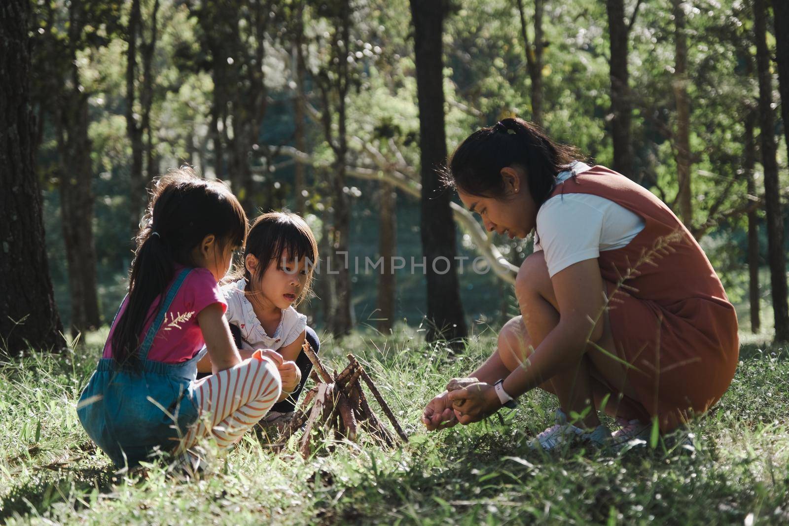 Mother and two daughters collecting firewood and kindling bonfire at camping place in forest. Family and children making campfire on nature woods. Family camping, spending time together on vacation. by TEERASAK