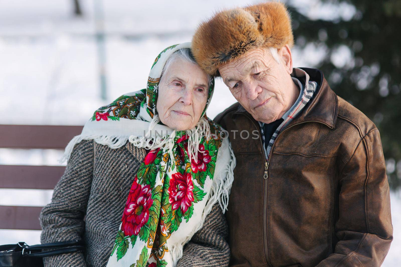 Senior people sitting on the bench in the park. Happy elderly couple spend time outside in winter by Gritsiv