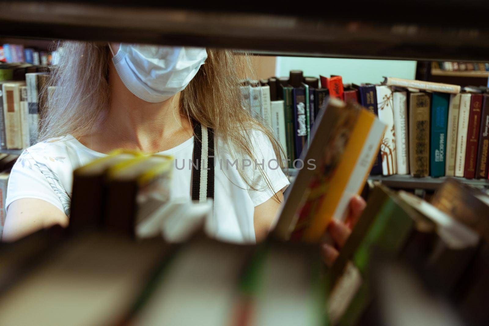 a girl in a mask looking for the right book in the library