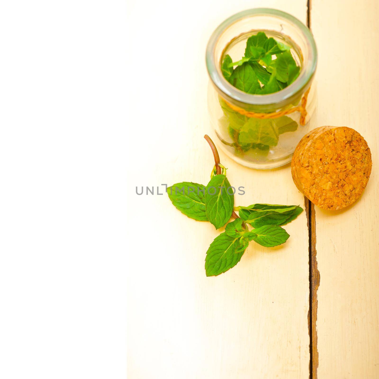 fresh mint leaves on a glass jarover a rustic white wood table