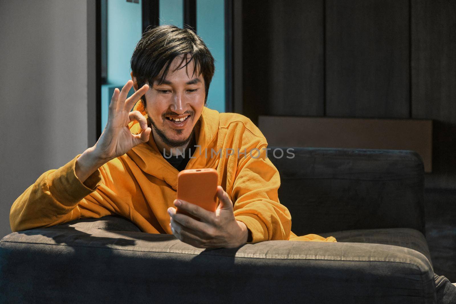 An Asian guy sits on sofa in a small office and communicates by mobile phone by snep_photo