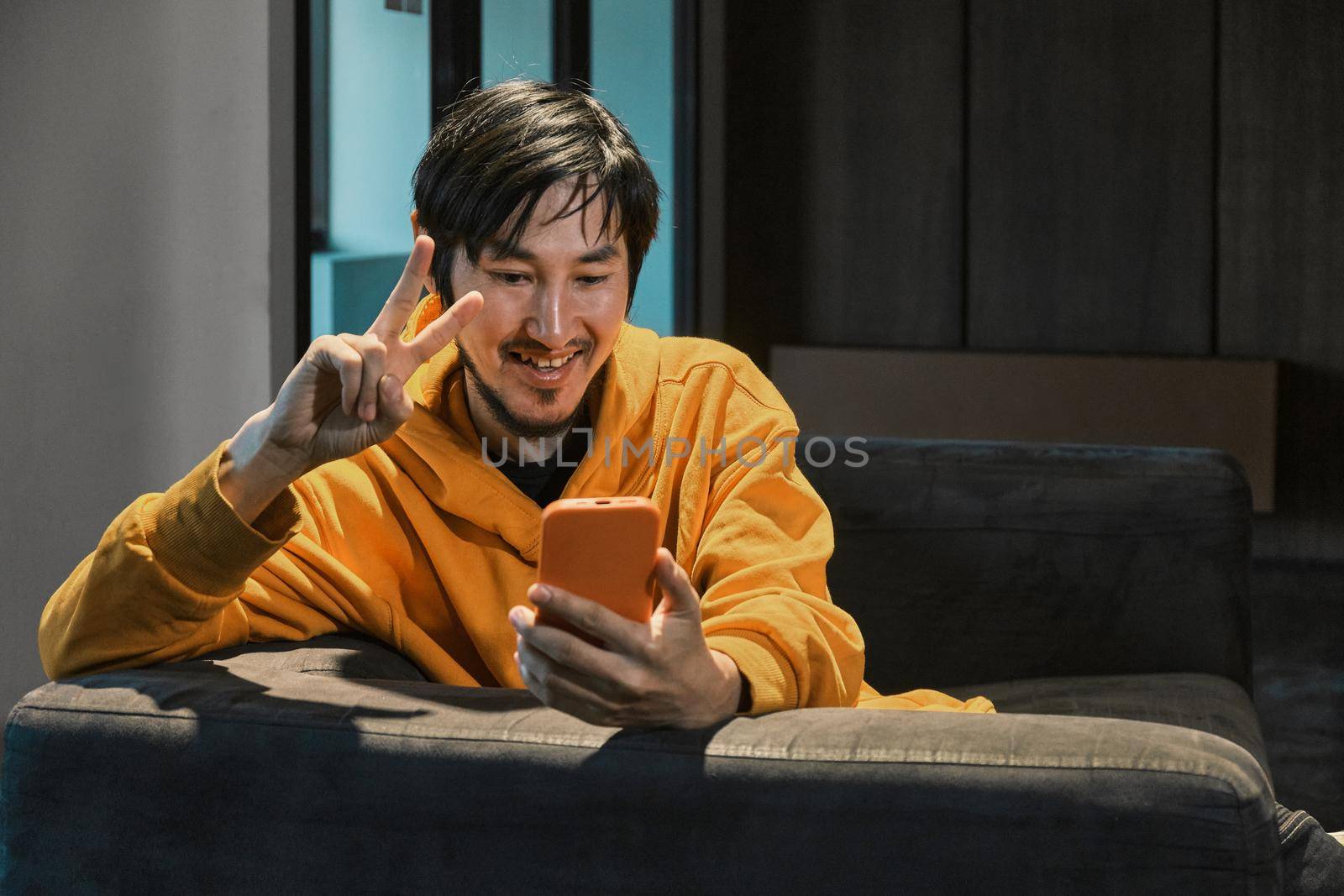 An Asian guy sits on sofa in a small office and communicates by mobile phone. The concept of small business and online communication.