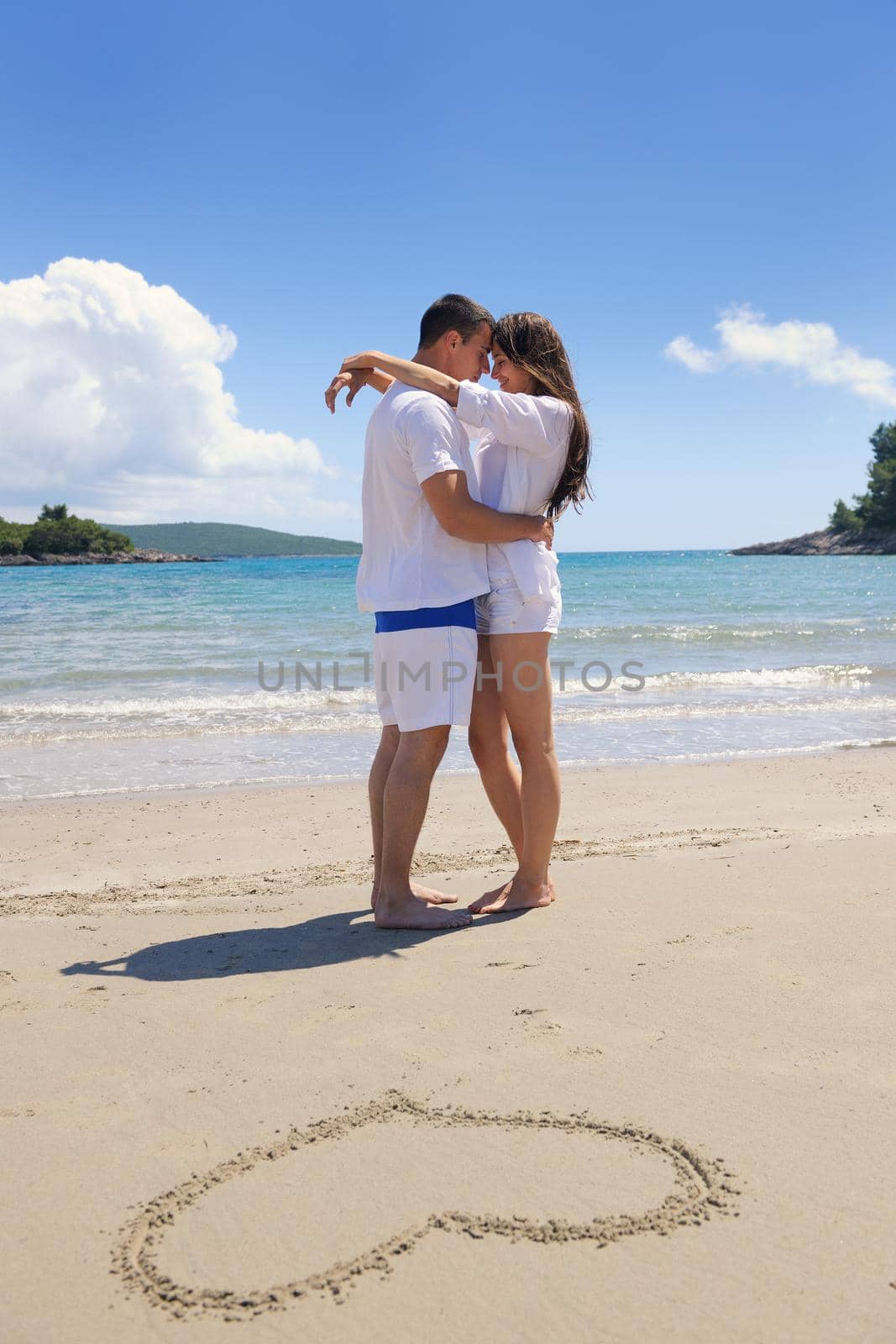 happy young couple have fun and relax  on the summer with heart drawing on beach sand