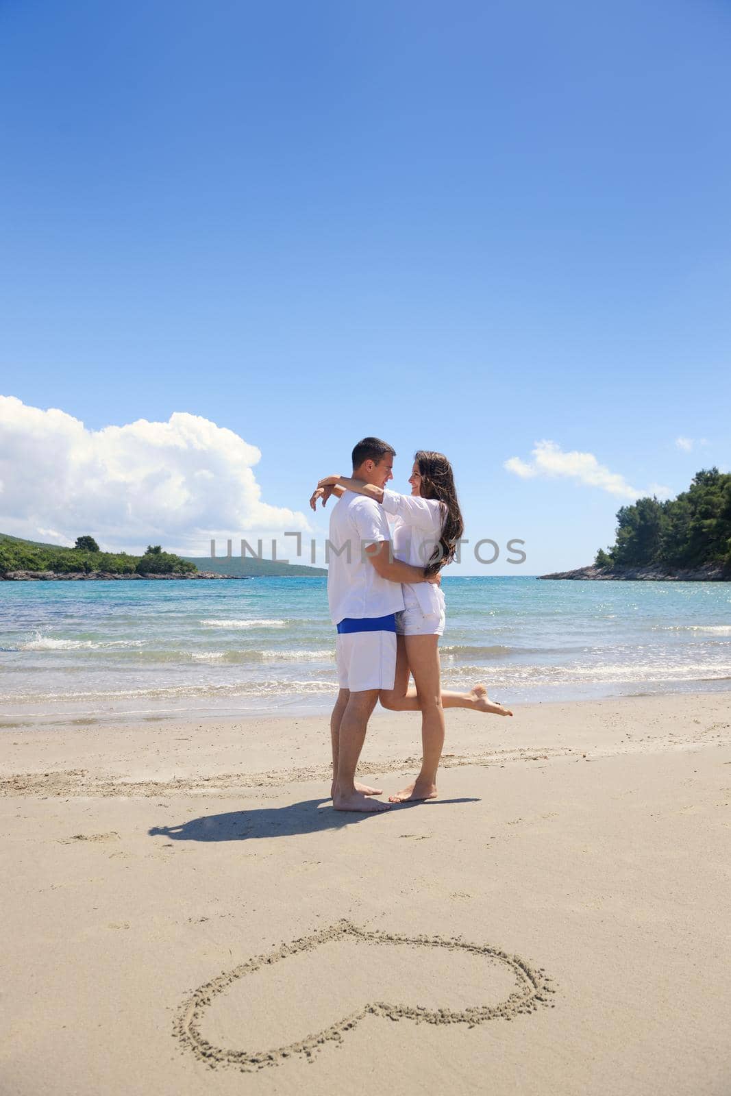 happy young couple have fun and relax  on the summer with heart drawing on beach sand