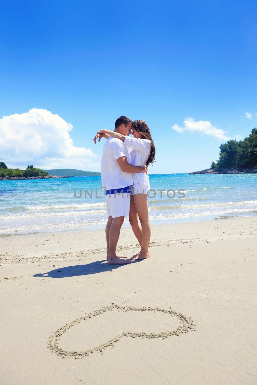 happy young couple have fun and relax  on the summer with heart drawing on beach sand