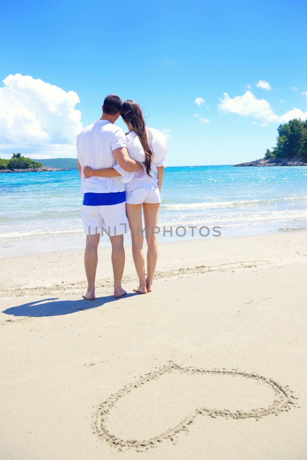 happy young couple have fun and relax  on the summer with heart drawing on beach sand