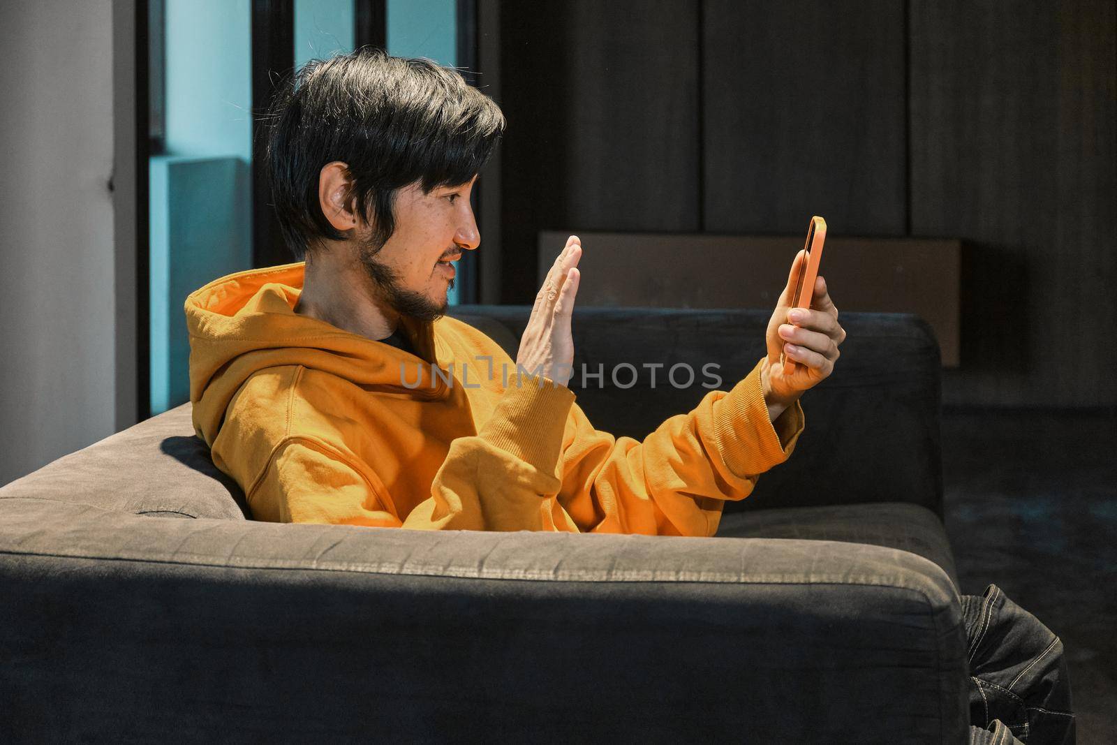 An Asian guy sits on sofa in a small office and communicates by mobile phone by snep_photo