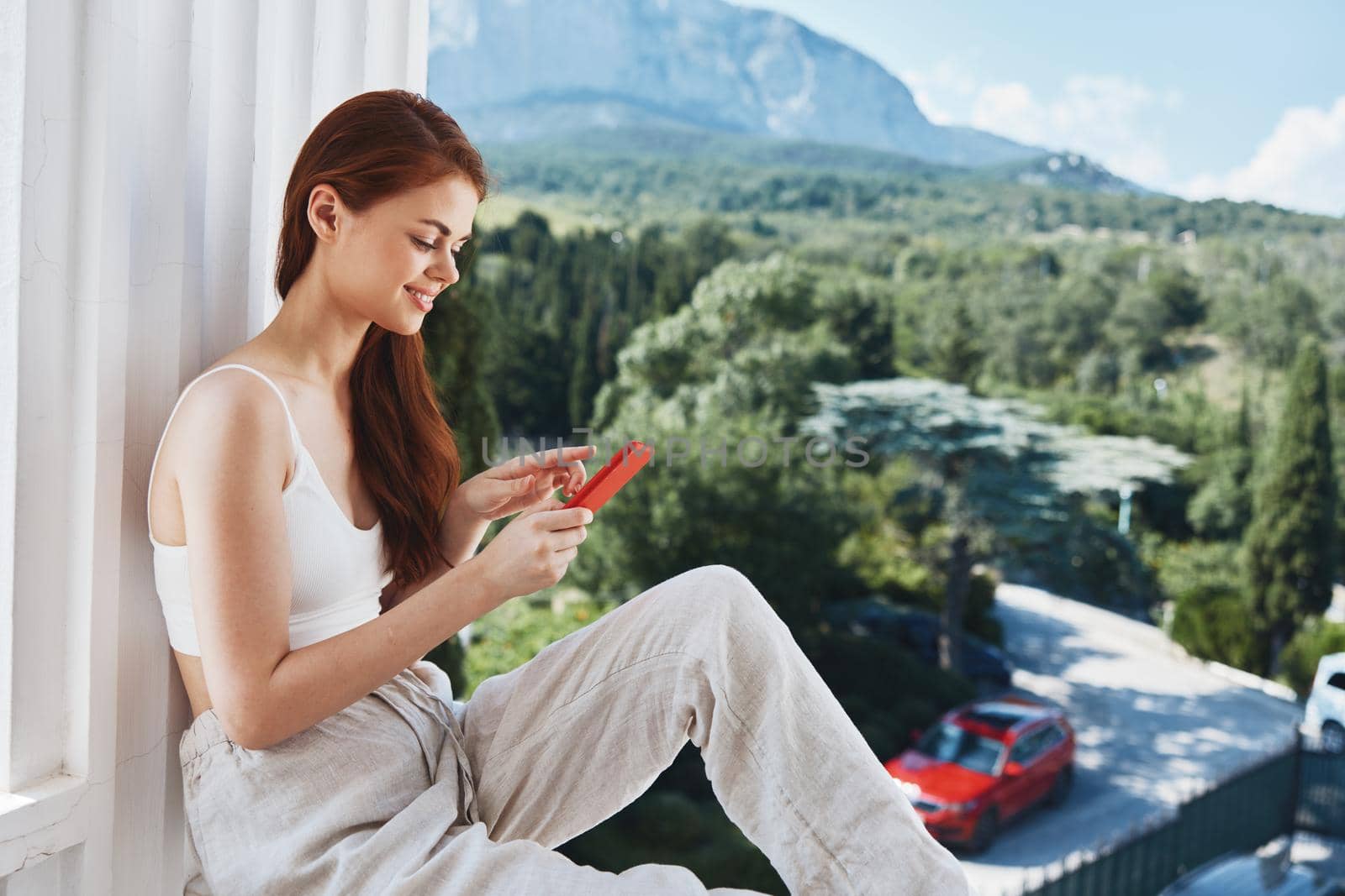 Portrait of gorgeous woman use the phone looks at the screen in a comfortable hotel an open view of the Perfect sunny morning. High quality photo