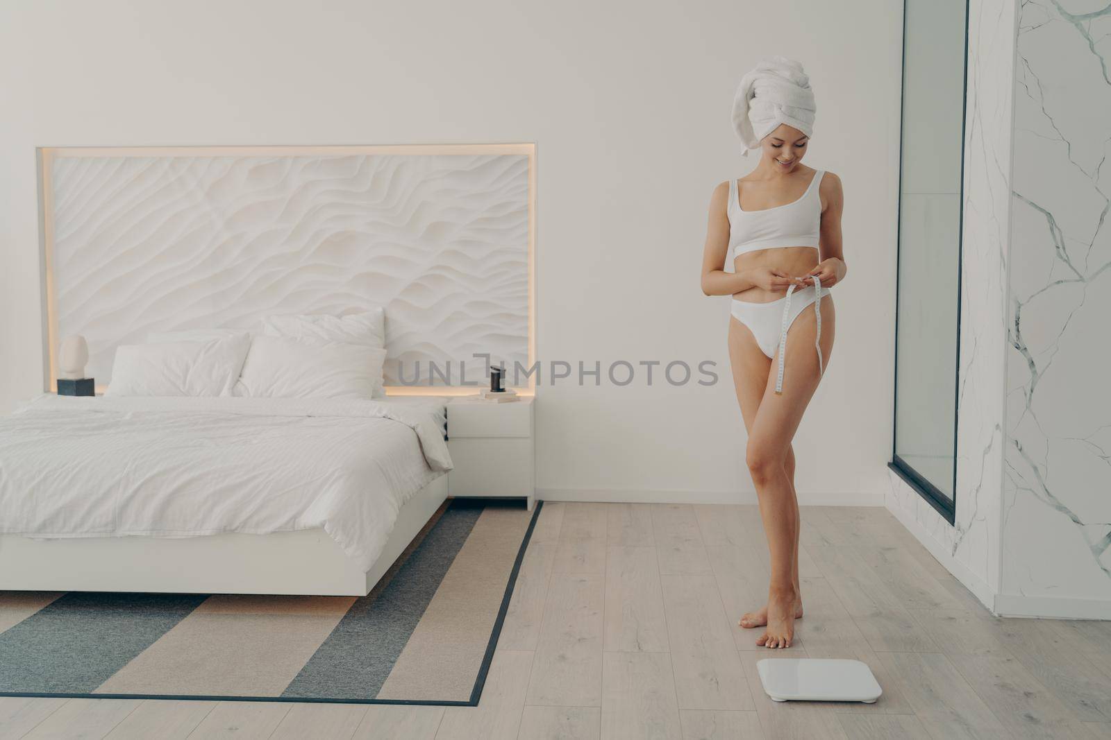 Beautiful slim fit female model posing in white underwear with measuring tape in hand by vkstock