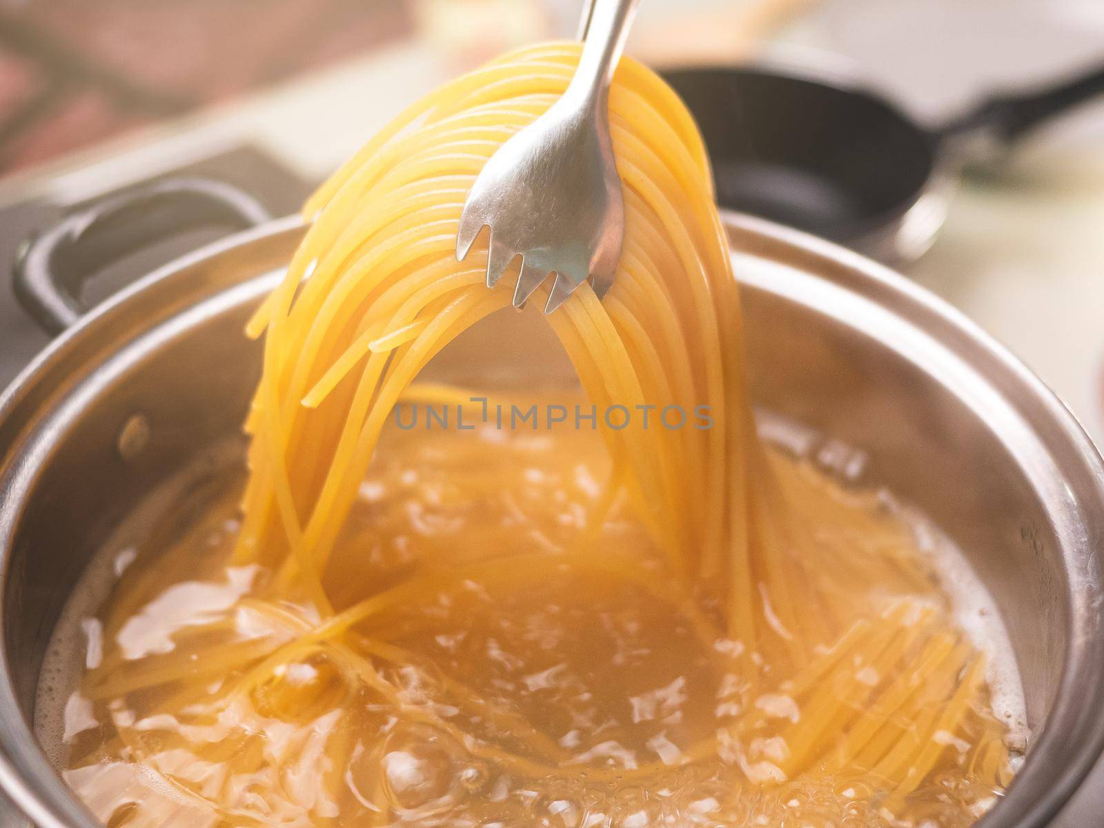 Raw spaghetti is being cooked in boiling water in a kitchen pot. Healthy Italian Food and Cooking concepts.