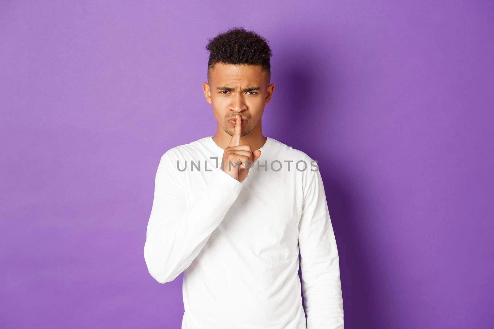 Image of angry african-american man hushing at you, press finger over lips, showing taboo sign, standing disappointed over purple background by Benzoix