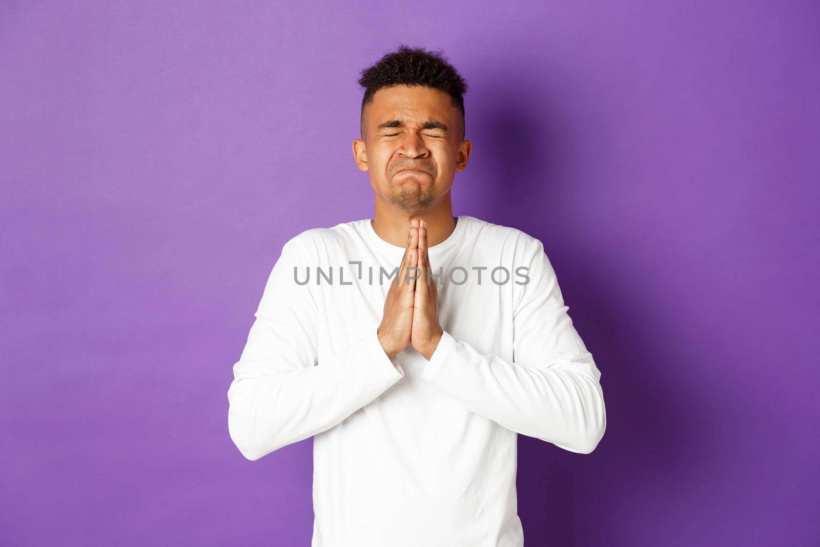 Image of desperate african-american guy pleading to God, holding hands in pray and begging for something, making wish, standing worried and asking for help.