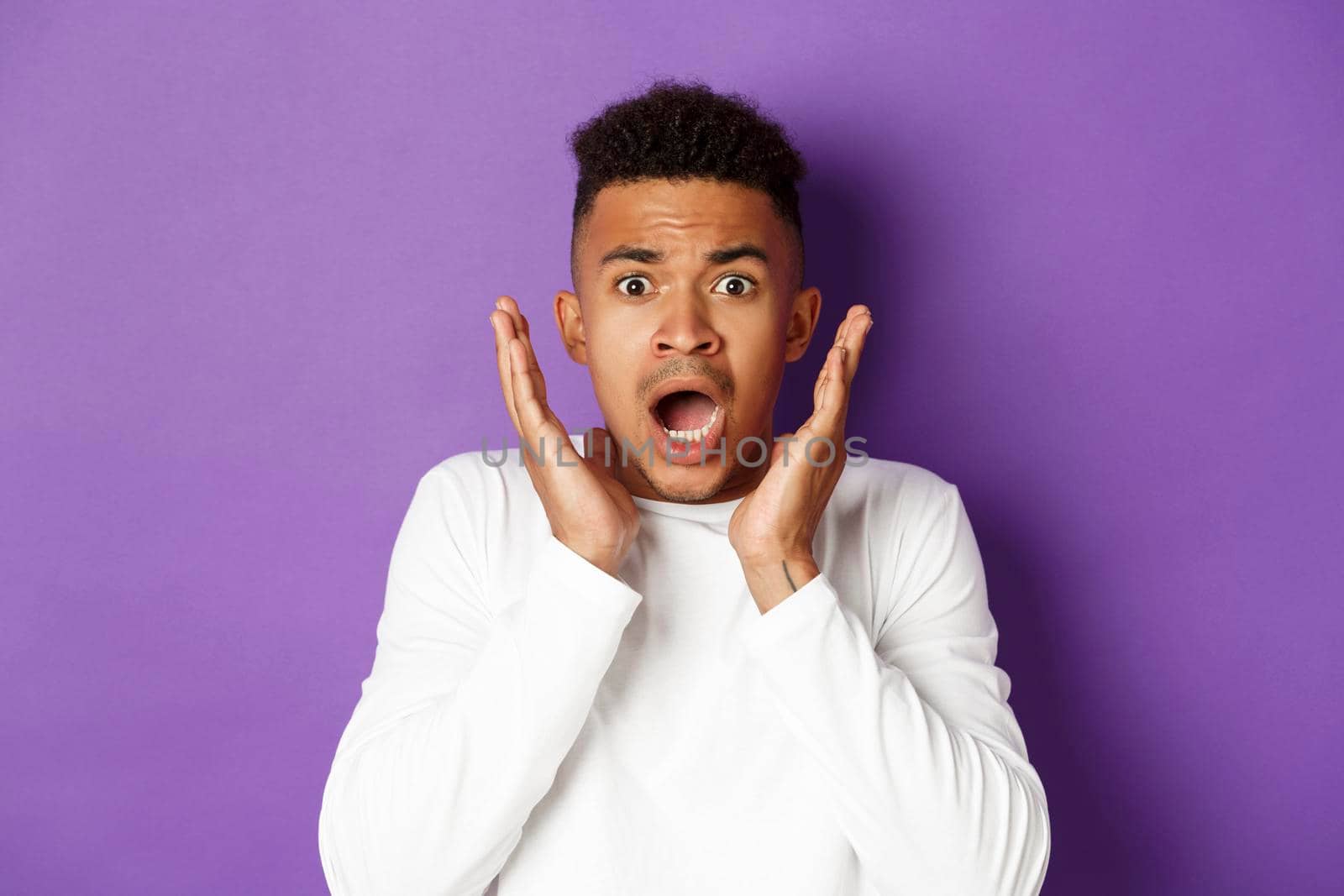 Closed-up of shocked and scared african-american man, gasping and looking startled at something bad, standing over purple background.