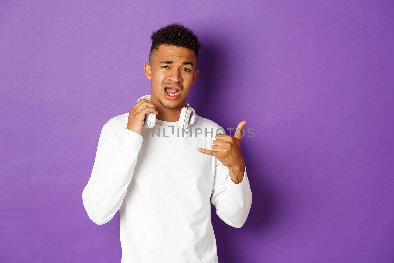 Image of sassy and cool african-american man, take-off headphones and showing hip hop gesture, standing over purple background.