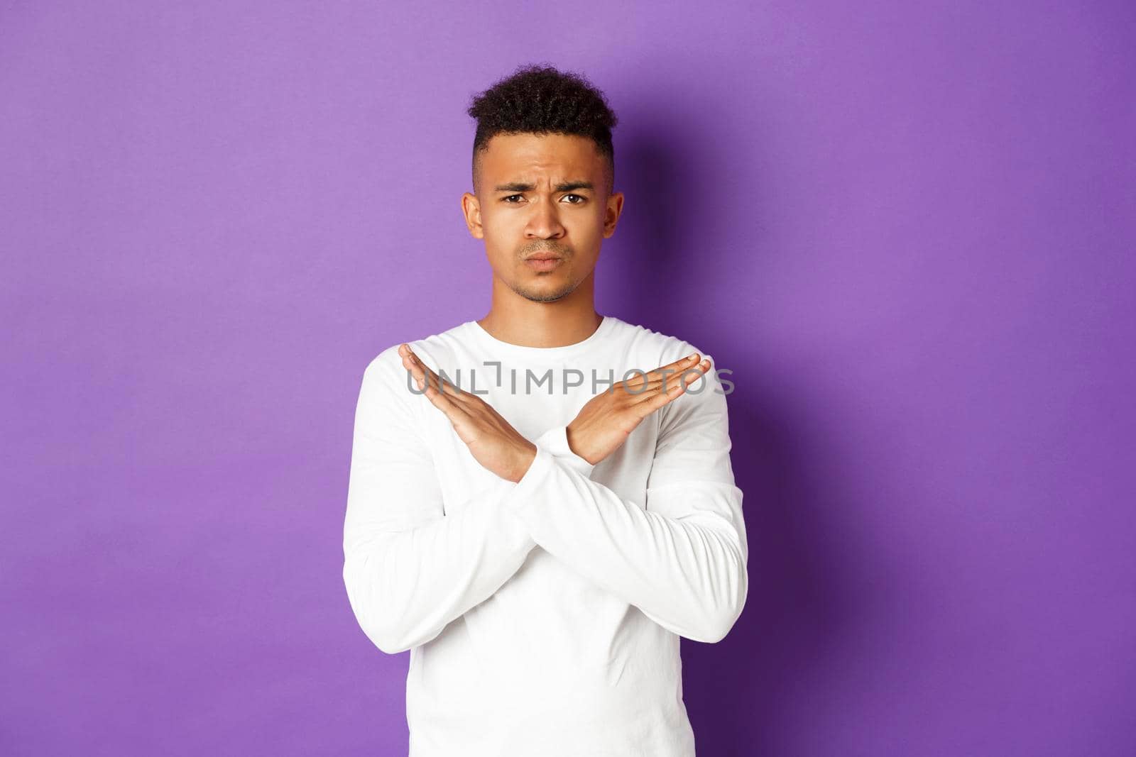 Image of upset african-american man, frowning and feeling disappointed, showing cross sign, tell to stop or disagree, standing over purple background.