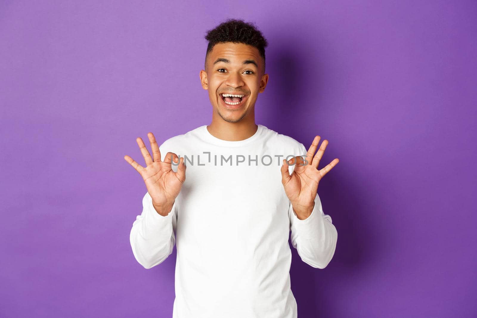 Image of satisfied african-american guy showing okay signs, being pleased with something, like and approve, standing over purple background.