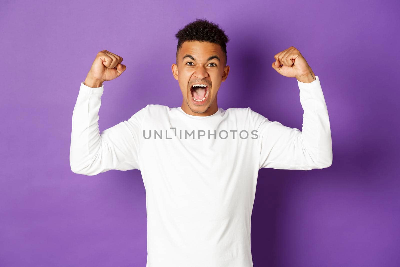 Image of encouraged african-american guy, shouting and looking determined, winning something, achieve goal and celebrating victory, standing over purple background by Benzoix