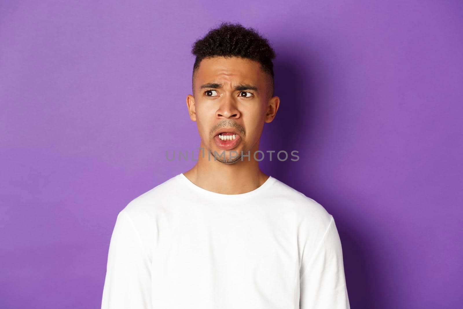 Image of shocked and startled african-american man, drop jaw and looking left at something embarrassing, standing over purple background by Benzoix