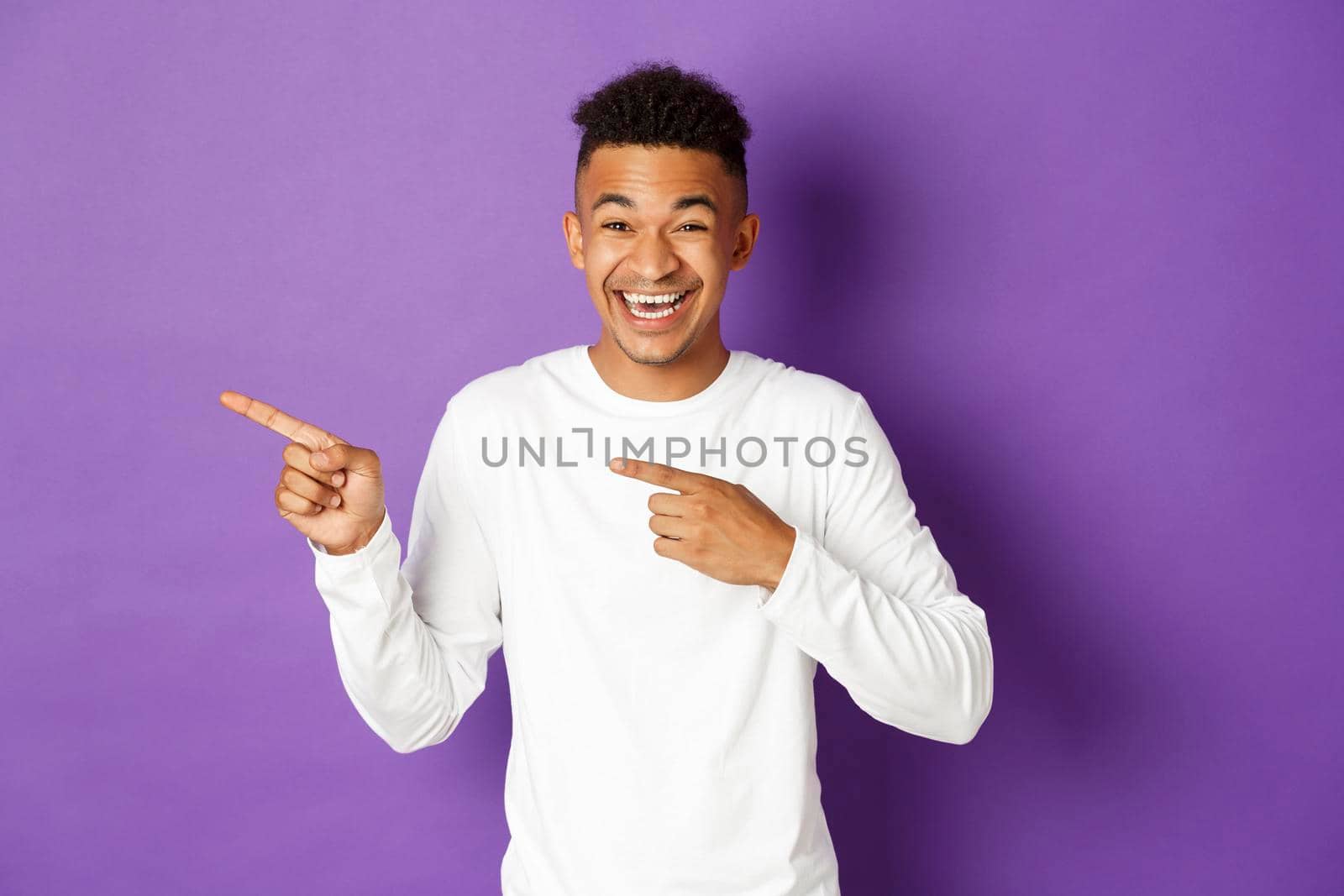 Image of handsome dark-skinned male model in casual outfit, pointing fingers left and laughing at funny advertisement, standing happy over purple background by Benzoix