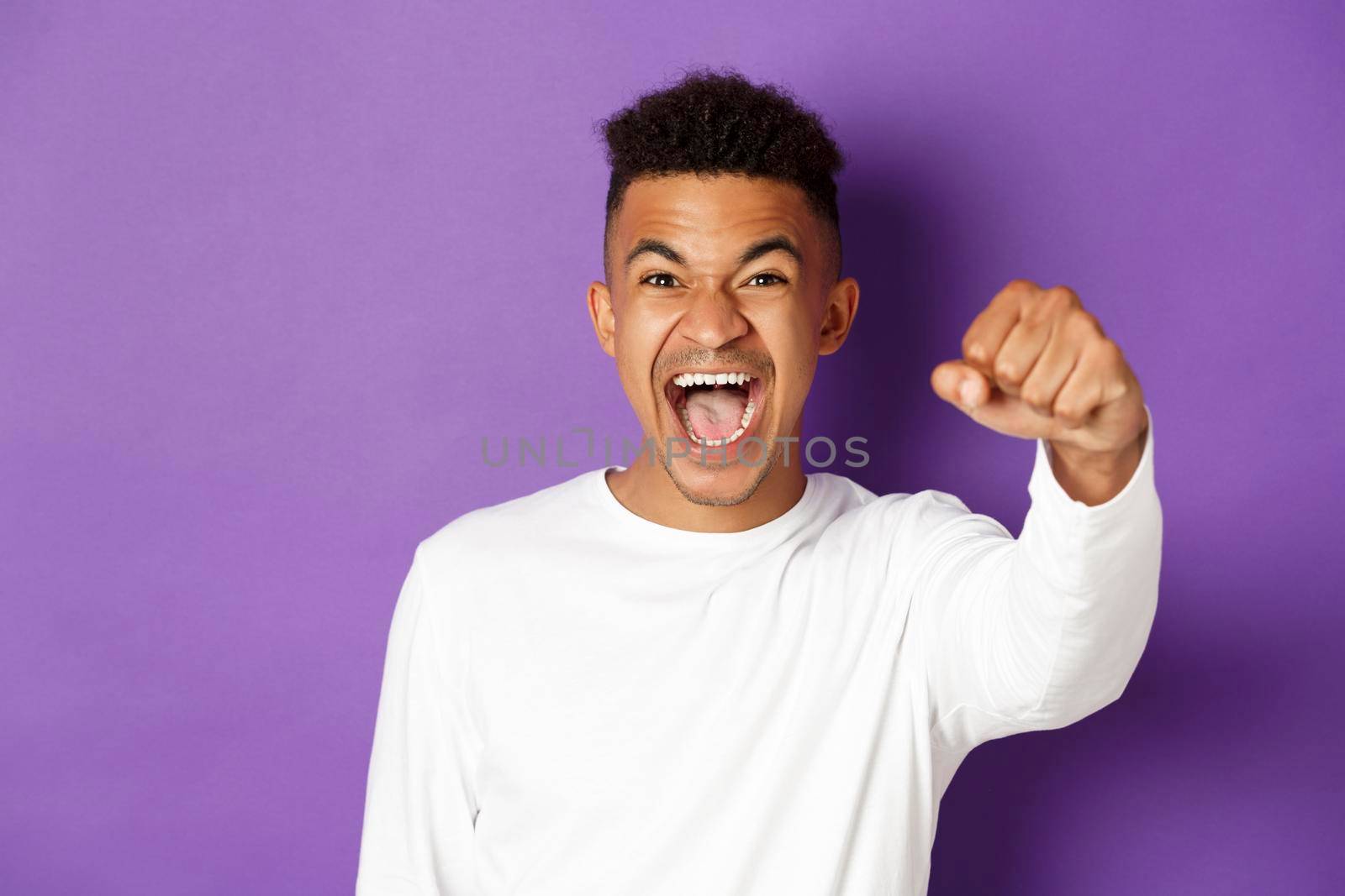 Close-up of determined and confident african-american man, raising fist and shouting black lives matter, fighting for his rights, standing over purple background by Benzoix