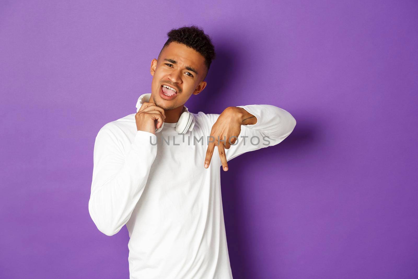Image of sassy and cool african-american man, take-off headphones and showing hip hop gesture, standing over purple background.