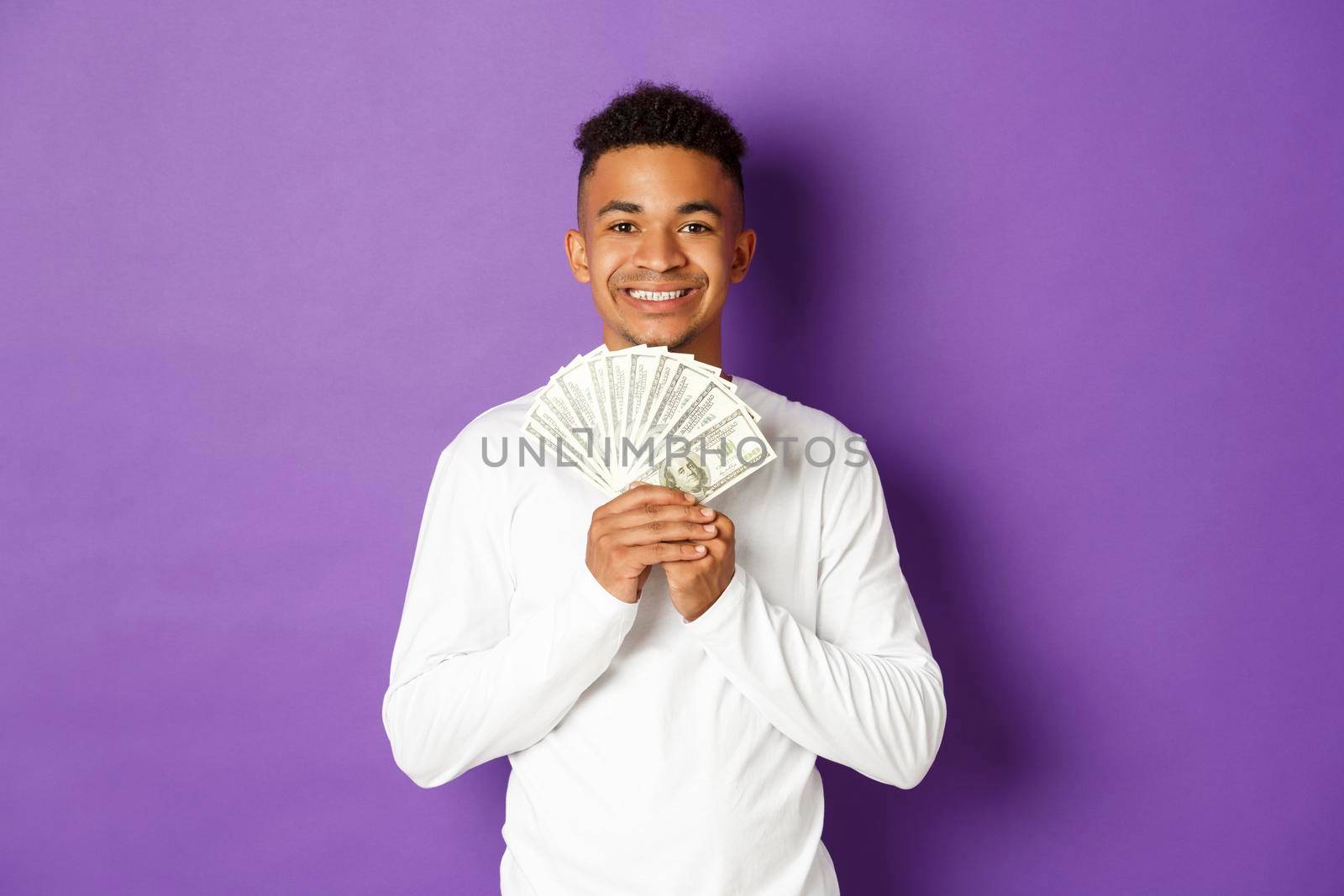 Portrait of handsome african-american man, showing money and smiling, got student loan, standing over purple background.
