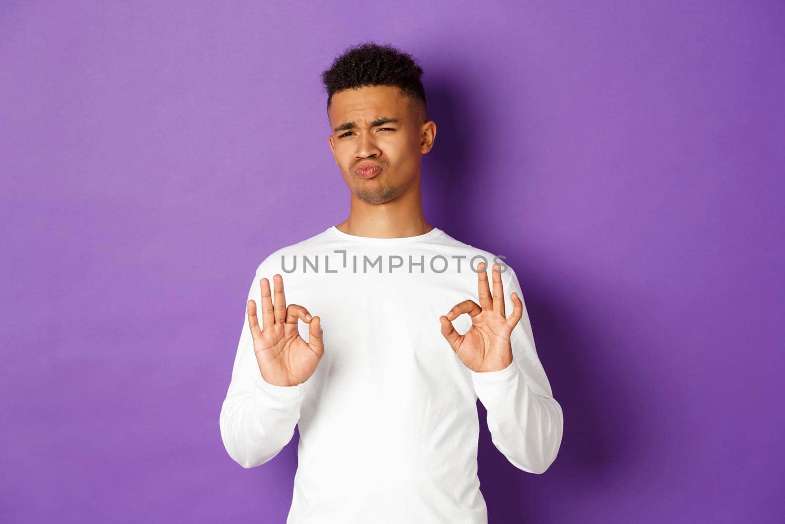 Satisfied handsome african-american man, showing okay signs and looking impressed, praise something good, standing over purple background.