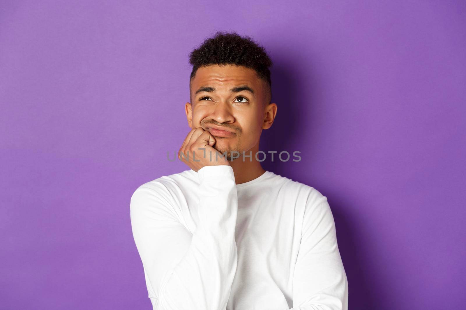 Close-up of indecisive african-american guy, sighing and looking up with perplexed and sad expression, standing over purple background by Benzoix