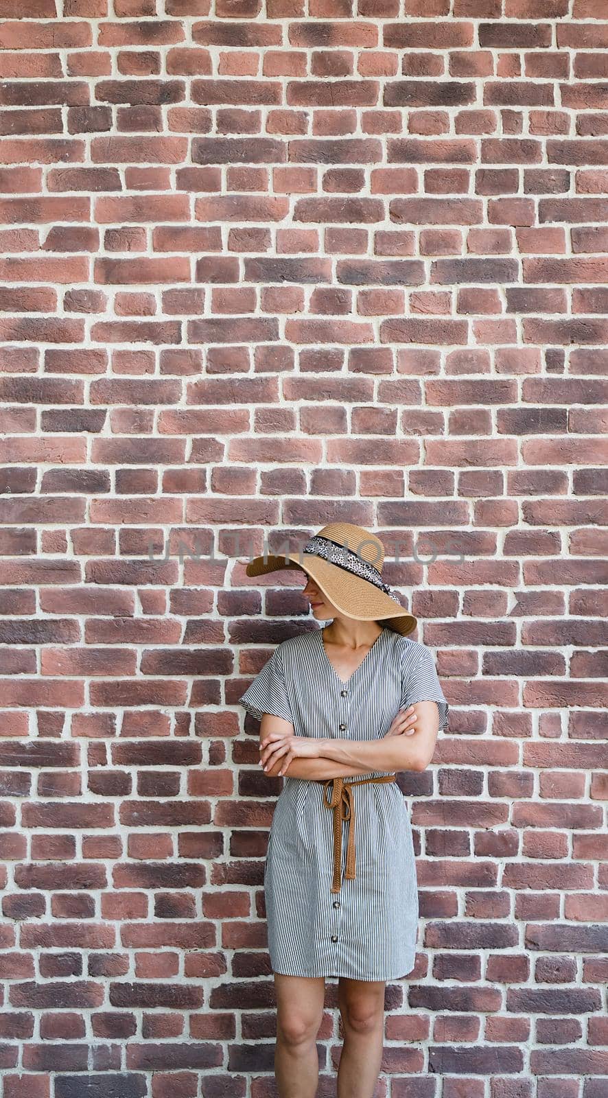 Summer style. Portrait of a beautiful young woman in summer dress and hat standing on red brick wall background