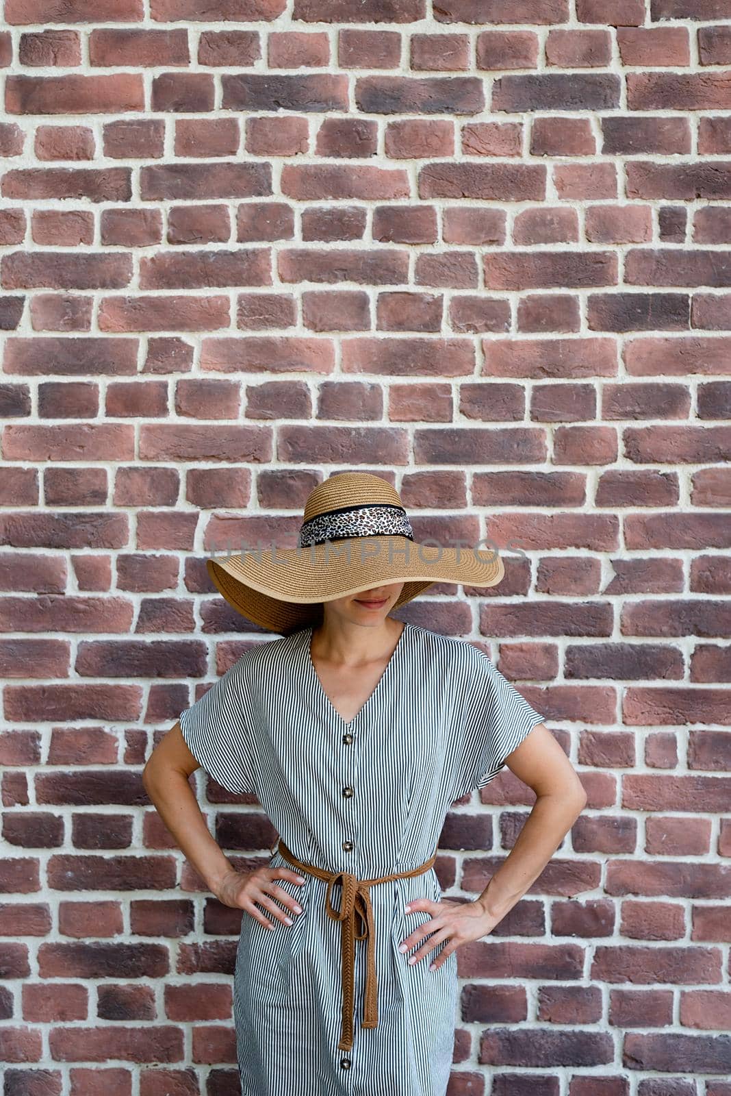 Summer style. Portrait of a beautiful young woman in summer dress and hat standing on red brick wall background