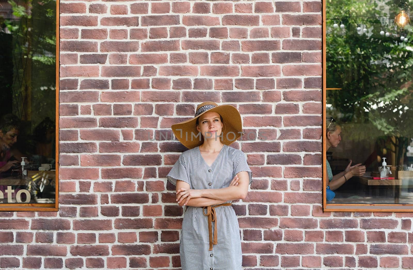 Summer style. Portrait of a beautiful young woman in summer dress and hat standing on red brick wall background