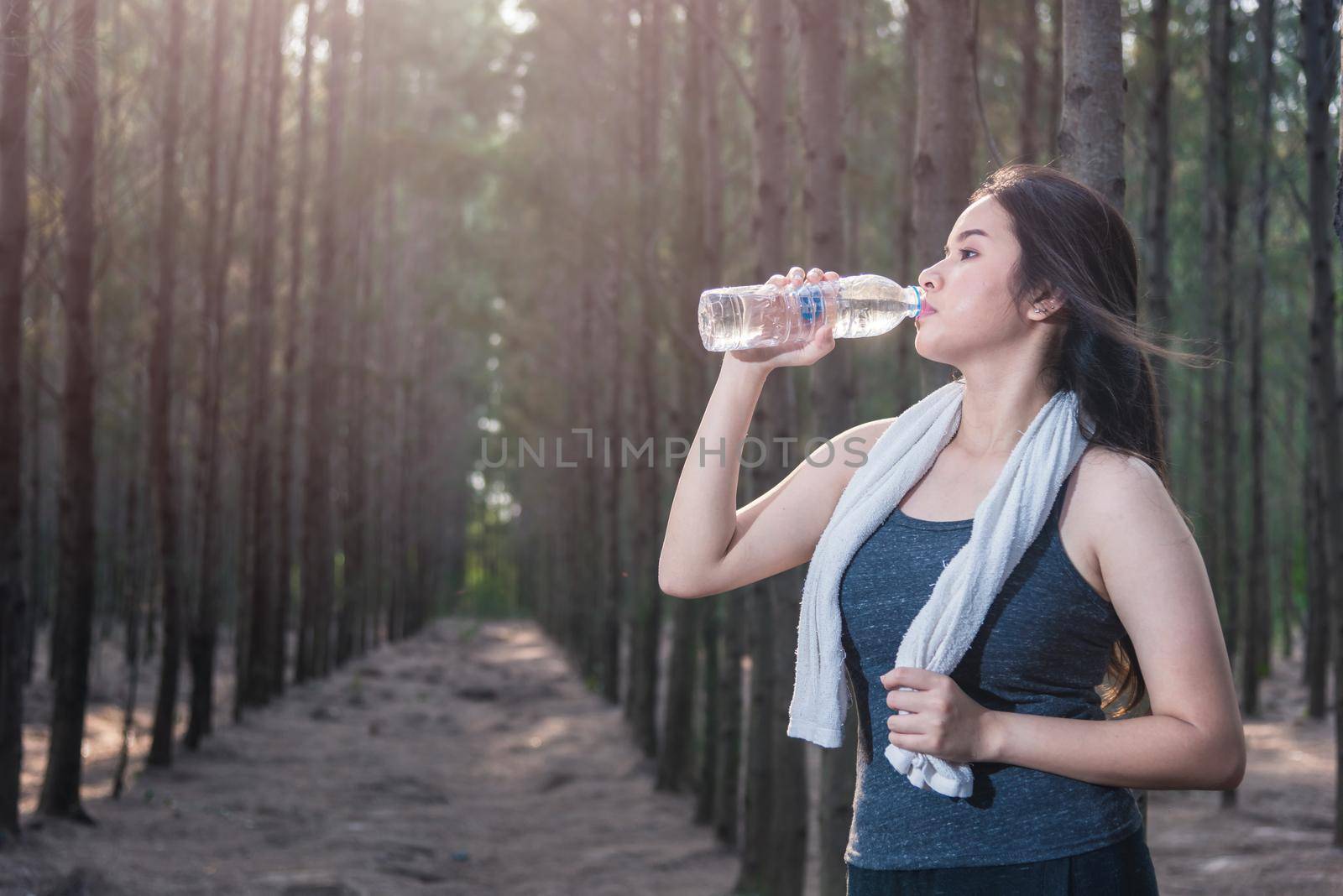 Beautiful young woman drinking water bottle after exercise fitness, in nature park forest