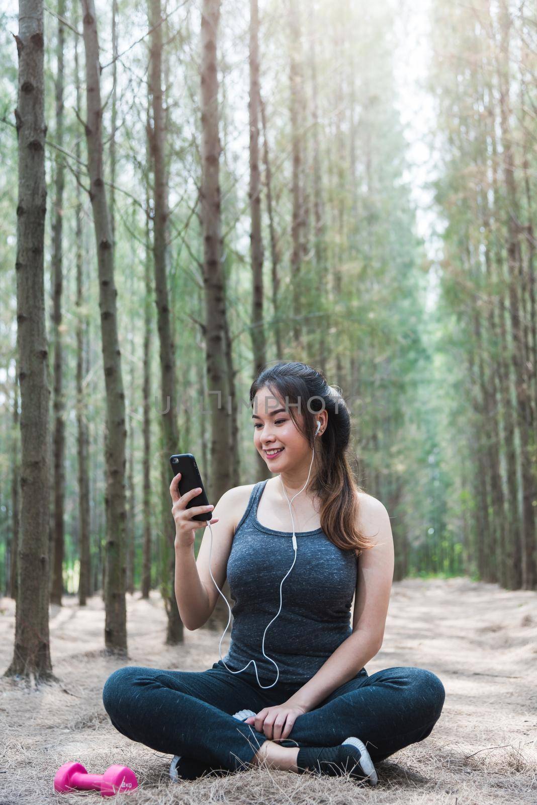 Sport happy young woman girl lifestyle exercise healthy using smart phone after dumbbell workout in forest nature park with copy space