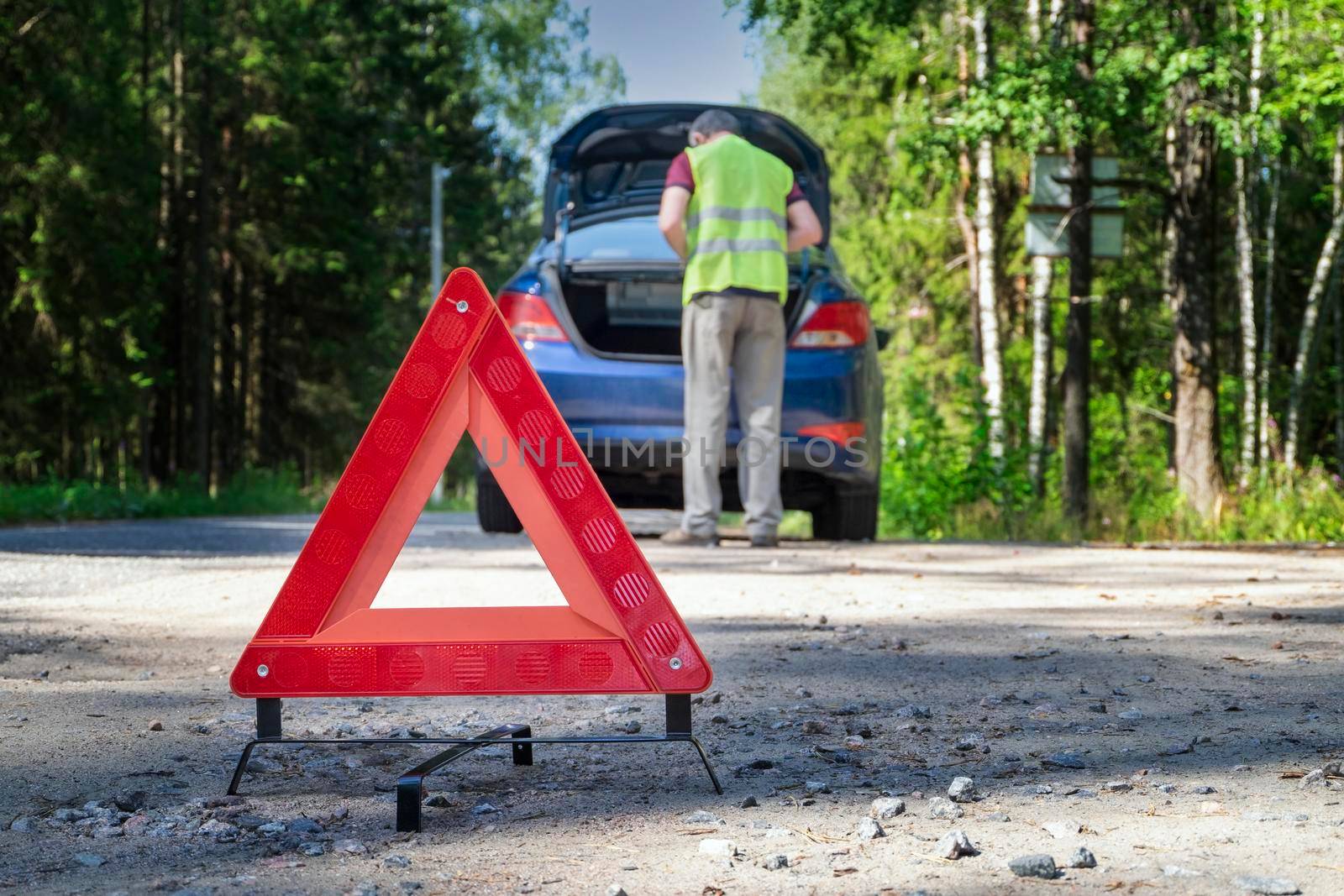 Red warning sign stands on the side of road next to damaged vehicle by OlgaGubskaya